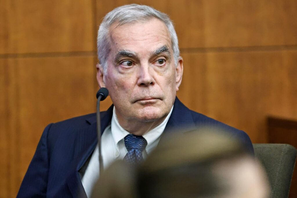 Forensic Psychiatrist Dr. Gregory Saathoff in the Clancy case sits in court with a normal looking blue suit and tie, white hair, and bushy eyebrows