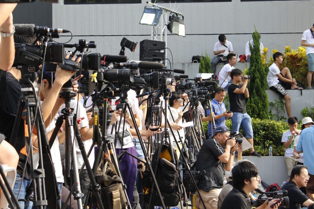 a large group of media members with big cameras are gather outside of a courthouse