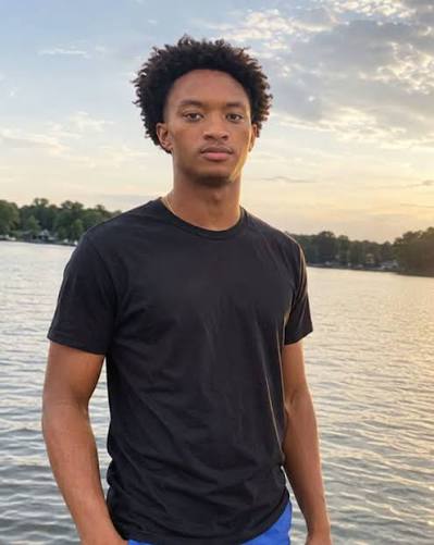 Nolan Wells in a black t-shirt standing at sunset by the water.