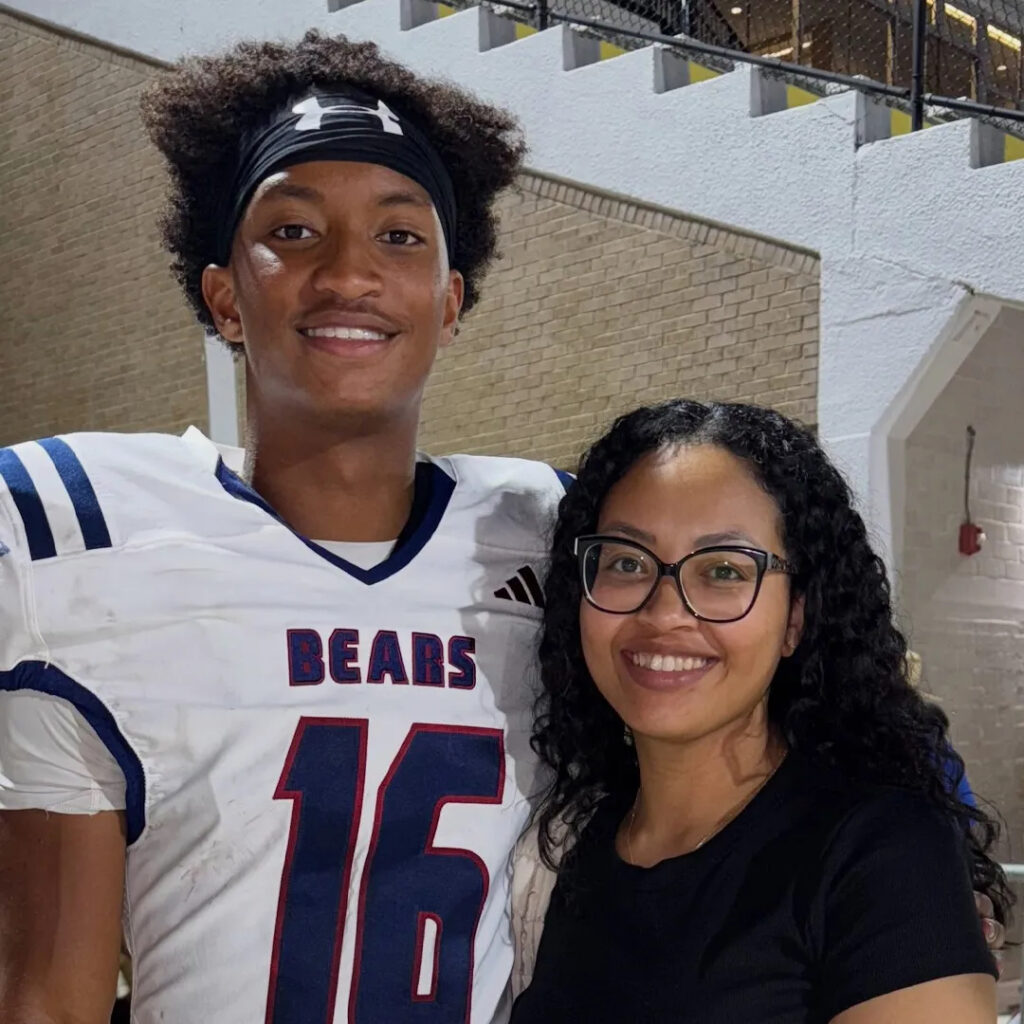 Nolan Wells and his Mother stand together smiling. Nolan is wearing his football uniform.