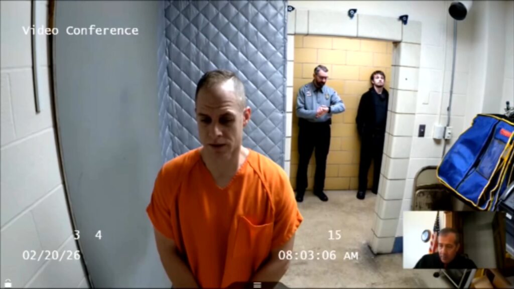 A split-screen legal broadcast showing Caleb Flynn in jail attire appearing on a video monitor to speak with a judge during a remote court proceeding.