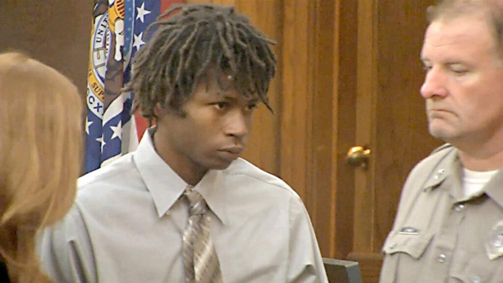 young black man in court with dreadlocks wearing aa brown button up shirt and tie.