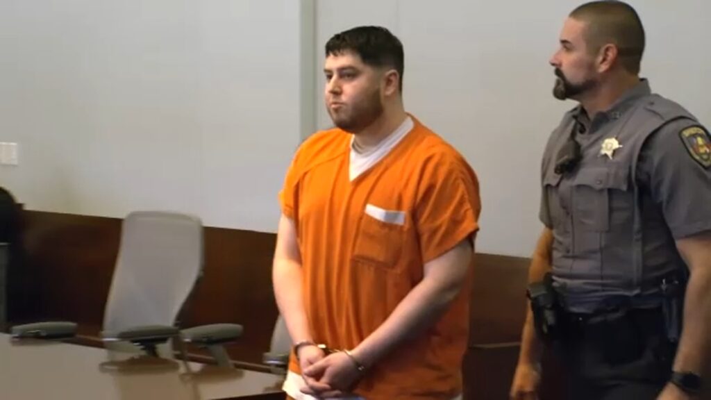 A courtroom photograph showing defendant Miguel Enrique Salguero-Olivares seated or standing next to his legal defense team inside a Durham County courthouse. He wears civilian or jail attire as legal proceedings take place.