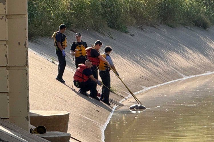 Emergency emergency personnel, including Houston fire and police units, gather near a bike path during the day along the water at White Oak Bayou to conduct recovery operations.